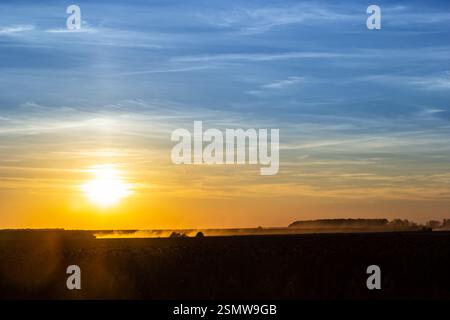 Una splendida alba illumina l'orizzonte con colori caldi, diffondendo una luce delicata sui campi nebbiosi. Questo momento sereno cattura la calma della natura di giorno Foto Stock