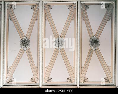Pannello soffitto decorato con design neoclassico simmetrico, caratterizzato da motivi intricati, modanature decorative ed elementi geometrici in tonalità beige. Elegante dettaglio architettonico con un'estetica vintage. Foto Stock
