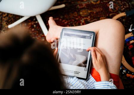 Parigi, Francia - 11 giugno 2023: Una donna seduta comodamente legge su Apple Vision Pro su un tablet, esplorando la sua navigazione a mani libere con gli occhi, ha Foto Stock