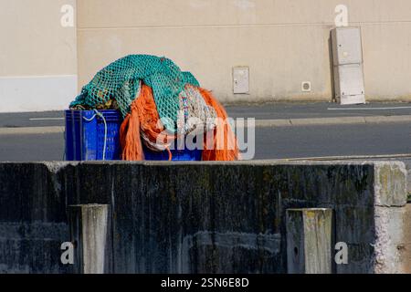 Una collezione di reti da pesca dai colori vivaci e attrezzature impilate sulla banchina del porto. Foto Stock