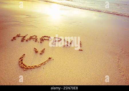 Messaggio felice scritto sulla sabbia vicino al litorale durante il tramonto sulla spiaggia Foto Stock