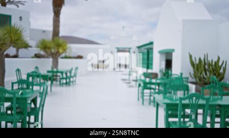 Vista sfocata di un patio all'aperto in stile coloniale messicano a lanzarote con sedie e tavoli verdi su uno sfondo bianco con palme Foto Stock