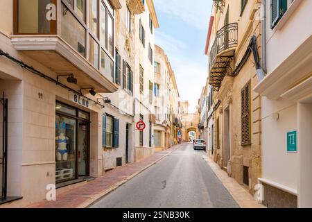 Una strada di appartamenti conduce allo storico Portal de San Roque, l'antico arco delle mura della città vecchia di Mahón, l'isola di Minorca, Spagna. Foto Stock
