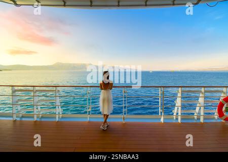 Una donna sta sul ponte di una nave da crociera al tramonto mentre naviga nel Mediterraneo passando per le isole greche vicino a Corfù in Grecia. Foto Stock