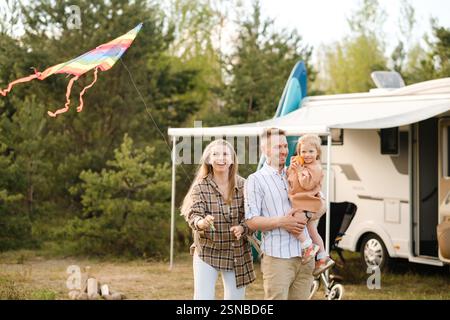 Una famiglia gioiosa vola con un aquilone colorato mentre si divertono all'aria aperta vicino al camper in un parco panoramico. Le Risate riempiono l'aria mentre celebrano un soleggiato da Foto Stock