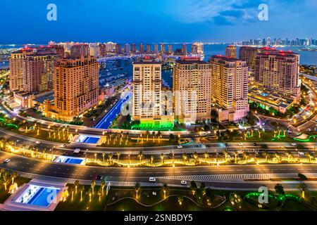 Vista panoramica notturna dall'alto dell'isola illuminata di Doha Pearl con lo skyline della città dietro il Golfo Persico a Doha, Qatar. Foto Stock