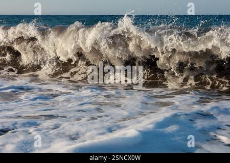 Un incredibile primo piano di una potente onda oceanica che si schianta sulla riva, con schiuma bianca e schizzi ghiacciati a mezz'aria Foto Stock
