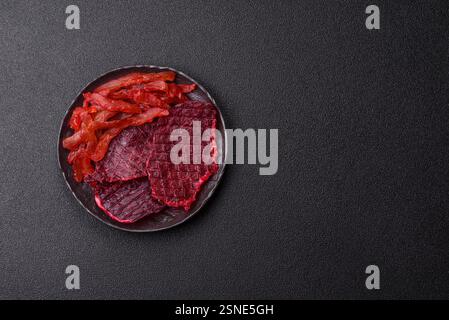 Fette di manzo essiccate, a scatti, con gusto di ciliegia o prugna, sale e spezie su sfondo di cemento scuro Foto Stock