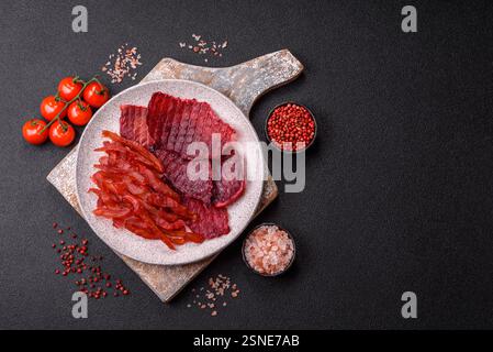 Fette di manzo essiccate, a scatti, con gusto di ciliegia o prugna, sale e spezie su sfondo di cemento scuro Foto Stock
