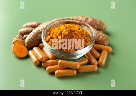 Polvere di curcuma in ciotola, radici e capsule su sfondo verde Foto Stock