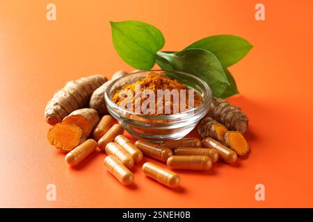 Polvere di curcuma in ciotola, radici e capsule su sfondo arancione, primo piano Foto Stock