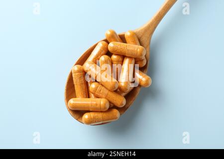 Capsule di curcuma in cucchiaio di legno su sfondo azzurro, vista dall'alto Foto Stock