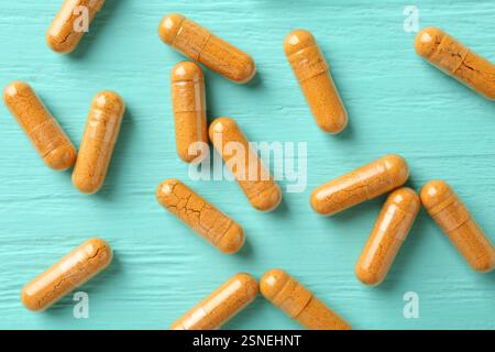 Capsule di curcuma su tavolo in legno turchese, piatto Foto Stock