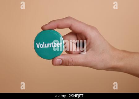 Uomo che tiene in mano il distintivo con la parola Volunteer su sfondo beige, primo piano Foto Stock