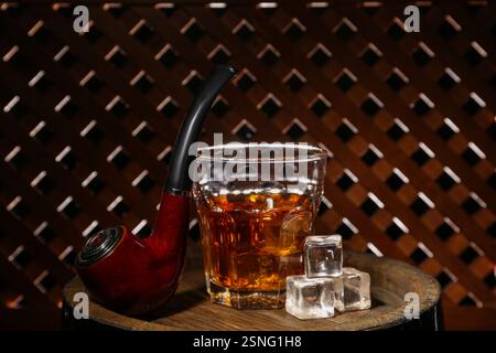 Bicchiere di rum con cubetti di ghiaccio e pipa da fumo vicino alla parete di legno Foto Stock
