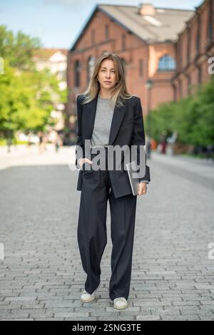 Elegante imprenditrice donna con laptop passeggia per le strade urbane, nomade digitale e freelance Foto Stock