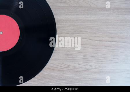 Disco in vinile nero con etichetta rossa su sfondo in legno, lasciando spazio vuoto per testo o design. Perfetto per musica, retrò e professionisti a tema nostalgico Foto Stock