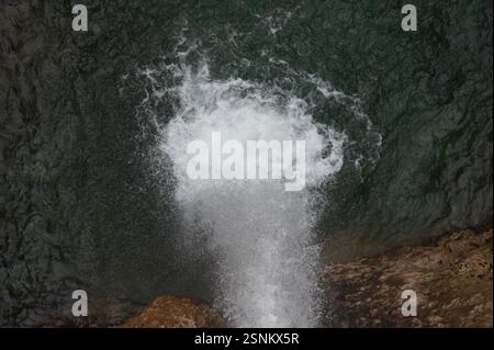 Un primo piano in Germania, Monaco rivela una cascata che scende giù da una scogliera rocciosa. L'acqua si schiude di bianco mentre rotola su rocce coperte di muschio, vetrina Foto Stock