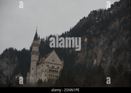 Un castello bianco con un'alta torre si trova in cima a una montagna innevata in Germania, Monaco, circondata da alberi. Castello di Neuschwanstein, famoso turista tedesco Foto Stock