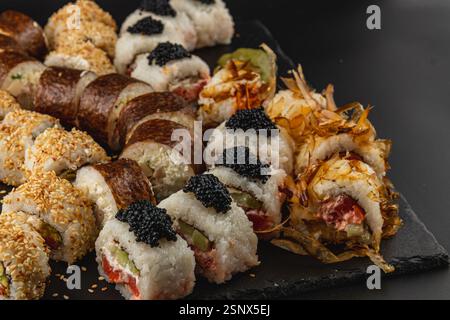 Una collezione di sushi roll assortiti disposti ad arte su un vassoio da portata in ardesia nera I colori e le texture vivaci attireranno chiunque voglia freschezza Foto Stock