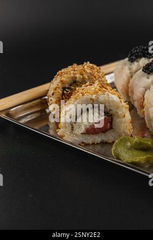 Deliziosi sushi roll sono disposti su un piatto metallico, con una varietà di ripieni. I panini sono guarniti con semi di sesamo e accompagnati Foto Stock