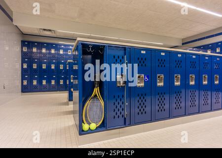 Armadietto per squadre vuoto, spogliatoio, spogliatoio, con un armadietto aperto contenente palle da tennis con racchette da tennis e tradizionali armadietti blu in metallo. Foto Stock