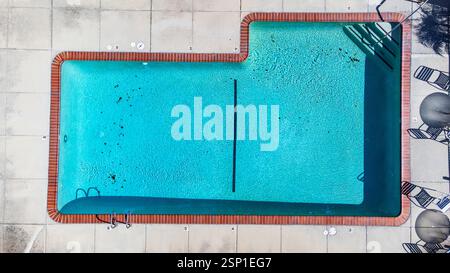 Vista aerea della piscina all'aperto con acque cristalline turchesi e detriti sparsi. Piscina delimitata da mattoni rossi e pavimentazione in cemento. Foto Stock