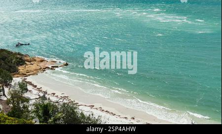 Una bellissima spiaggia con sabbia bianca e acque turchesi, dove le onde calme si infrangono dolcemente sulla riva. In lontananza, una piccola barca aggiunge alla scena serena, Foto Stock