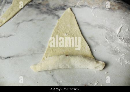 Un triangolo di pasta sfoglia cruda è avvolto in un croissant. Fare croissant. Foto Stock