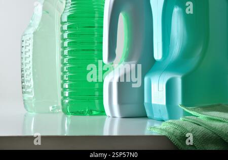 Fondo di quattro flaconi di plastica con prodotti disinfettanti per la pulizia di superfici diverse su un banco bianco e un panno in microfibra con isolamento bianco Foto Stock