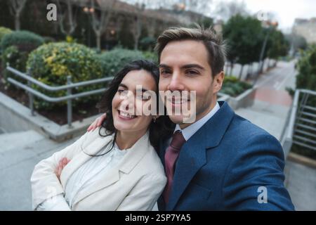 Una coppia d'affari sorridente che scatta selfie in un ambiente urbano Foto Stock