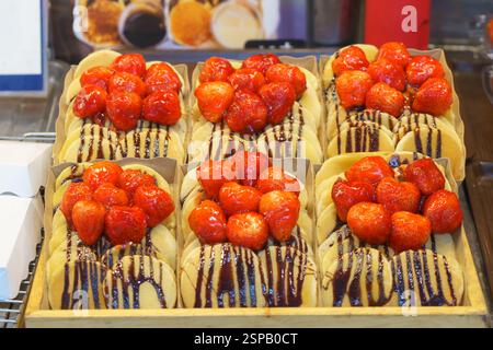 primo piano di mini frittelle appena preparate, ricoperte di fragole succose e condite con salsa al cioccolato. Questi dolcetti, esposti a un desse Foto Stock