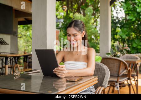 Giovane donna asiatica che lavora su un tablet digitale in un bar Foto Stock