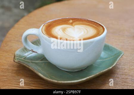 Una tazza di cappuccino con latte art a forma di cuore isolato su tavolo di legno Foto Stock