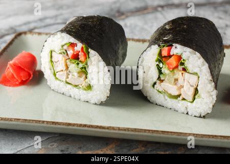 Sushi burrito o sushirrito con pollo alla griglia, riso, formaggio spalmabile, cetriolo, peperone, primi piani di nori e lattuga in un piatto sul tavolo. orizo Foto Stock