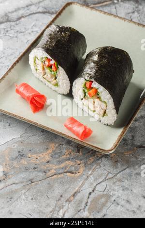 Sushi burrito con cucina fusion con riso, pollo, formaggio spalmabile, verdure e lattuga da vicino in un piatto sul tavolo. Verticale Foto Stock