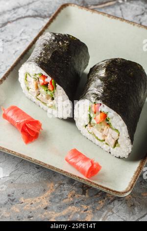 Burrito sushi fresco con riso, pollo, formaggio spalmabile, verdure e lattuga avvolti in alghe nori da vicino in un piatto sul tavolo. Verticale Foto Stock