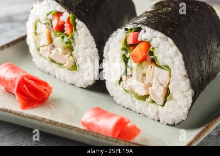 Delizioso burrito sushi con riso, pollo, formaggio spalmabile, verdure, nori e lattuga da vicino in un piatto sul tavolo. orizzontale Foto Stock