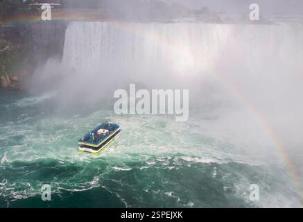 Un tour in barca si avvicina alla base delle Cascate del Niagara, circondato dalla nebbia e che mostra un vibrante arcobaleno in alto. Foto Stock
