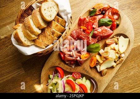 Un tagliere rustico di salumi con un assortimento di affettati, formaggi, insalata fresca con pomodori e cetrioli e un cestino di pane a fette. Il Foto Stock