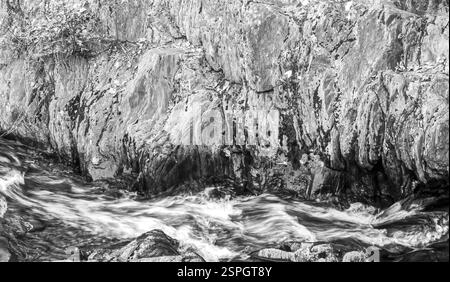 Una fotografia monocromatica di una superficie di roccia testurizzata con acqua che scorre sulla superficie, catturando il contrasto tra movimento e quiete. Foto Stock