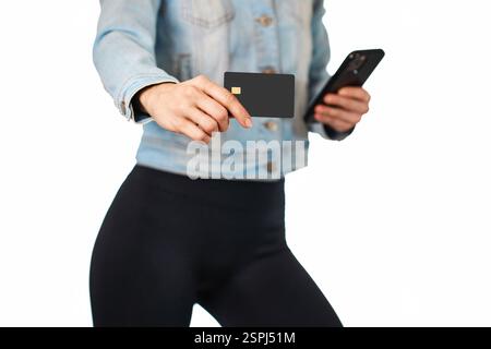 donna in denim con cellulare e carta di credito premium nera su sfondo bianco. donna che paga con carta di credito di plastica sull'app per smartphone, Foto Stock