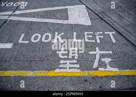 Guarda a sinistra, Warnhinweis auf dem Asphalt, Hong Kong, Volksrepublik Cina Foto Stock
