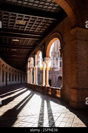 Un bellissimo corridoio architettonico con archi e intricati dettagli del soffitto, illuminato dalla luce del sole che proietta lunghe ombre sul pavimento piastrellato. Nella Foto Stock