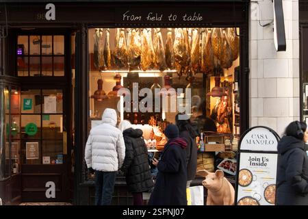 I clienti possono ammirare il prosciutto stagionato appeso alla finestra di Casa Manolo, un ristorante spagnolo di tapas al 99 Strand, Londra. Stanno pensando di cenare all'interno. Foto Stock