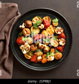 Verdure cotte al forno su piatto nero su sfondo scuro. Vista dall'alto, disposizione piatta Foto Stock
