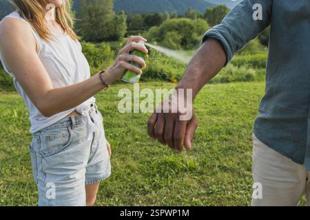 Una giovane coppia che spruzza repellente per zecche sulle gambe e sulle braccia durante un viaggio estivo nella natura Foto Stock