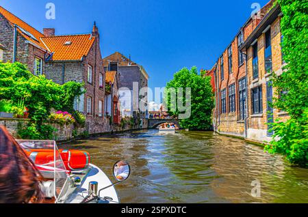 Canale d'acqua di Bakkersrei con barca turistica, ponte Mariabrug e edifici medievali mura con piante verdi nel centro storico di Bruges, Bruges City hi Foto Stock