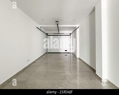 Garage minimalista con pareti bianche pulite, porta motorizzata e ampio spazio. Foto Stock
