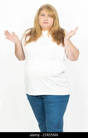 Ritratto di una donna bionda più dimensioni che fa un gesto di cespuglio con entrambe le mani. Indossa abiti casual, una t-shirt bianca e jeans blu. Foto Stock